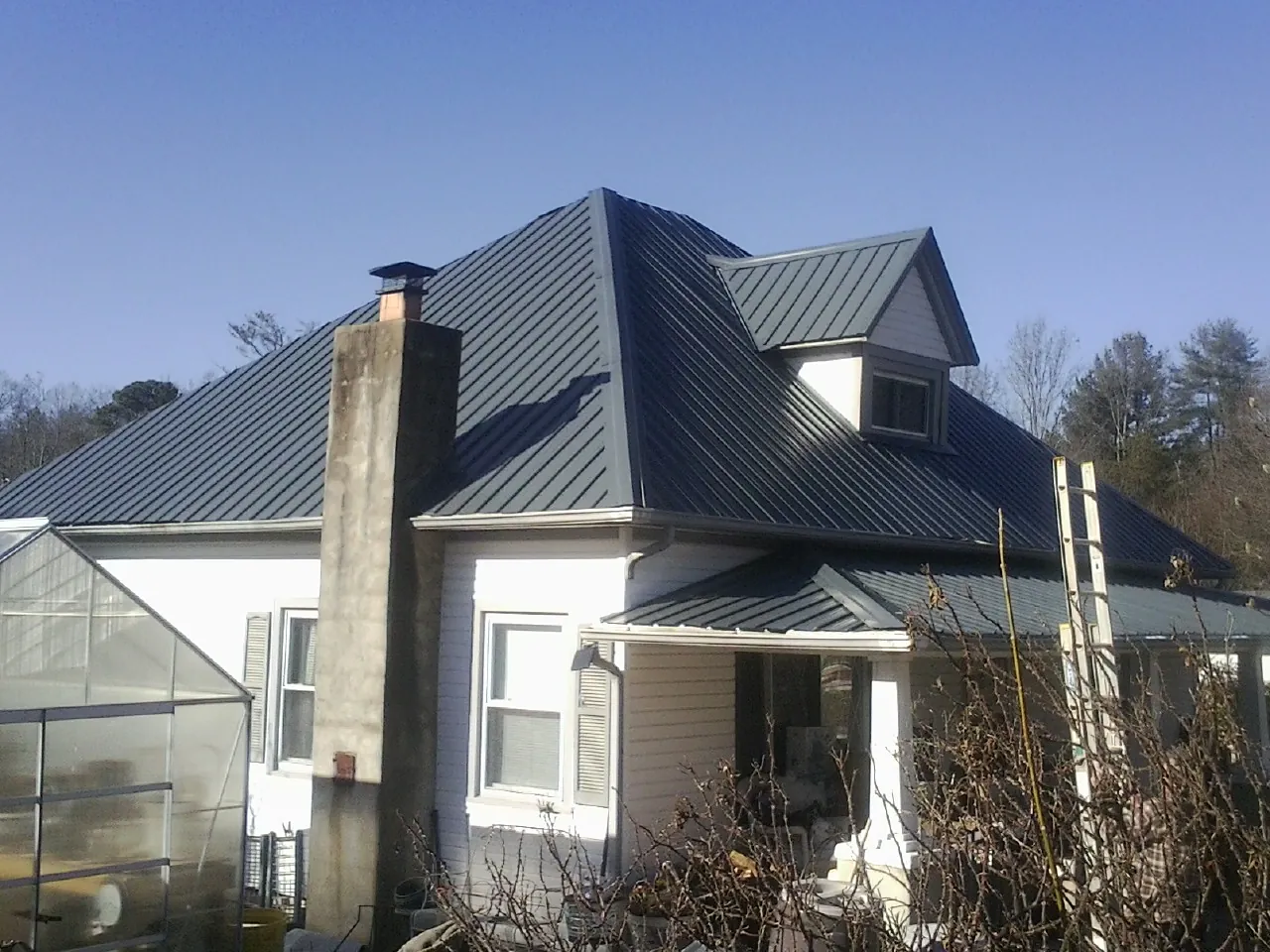 Dark blue standing seam metal roof on a white farmhouse with dormer — Slate & Tile Roof Repair by Roofing Brothers in Georges Mills
