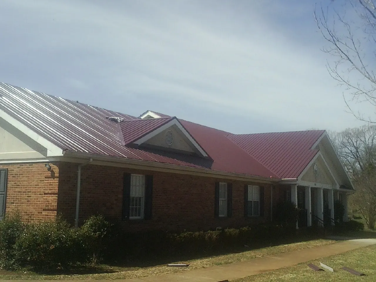 Red metal roof with gabled entries on a long brick building, from a Hail Damage Roof Repair job in Georges Mills