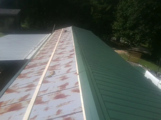 Old rusted panels beside newly installed green metal roofing — Wind Damage Roof Repair by Roofing Brothers in Georges Mills
