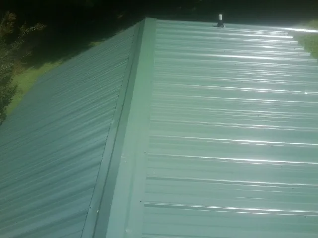 New green metal panels meeting at the ridge of a roof — Flat Roof Repair work by our crew in Georges Mills