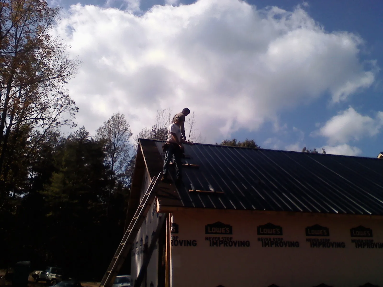 Roofer fastening dark metal panels high against a cloudy sky, from a Roof Inspection job in Georges Mills