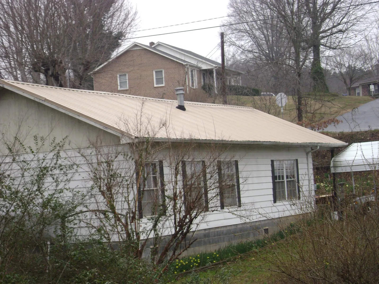 Tan metal roof on a white sided house set into a hillside — Commercial Roofing by Roofing Brothers in Georges Mills