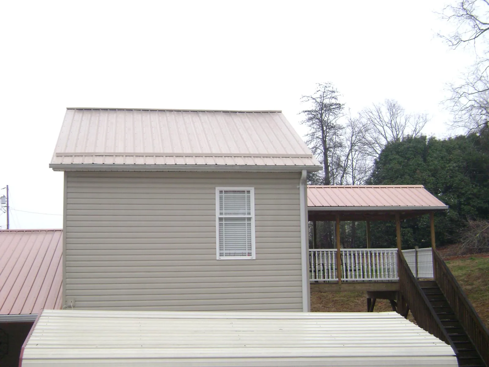 Tan metal roofs on a two story addition and attached porch, from a Roof Replacement job in Georges Mills